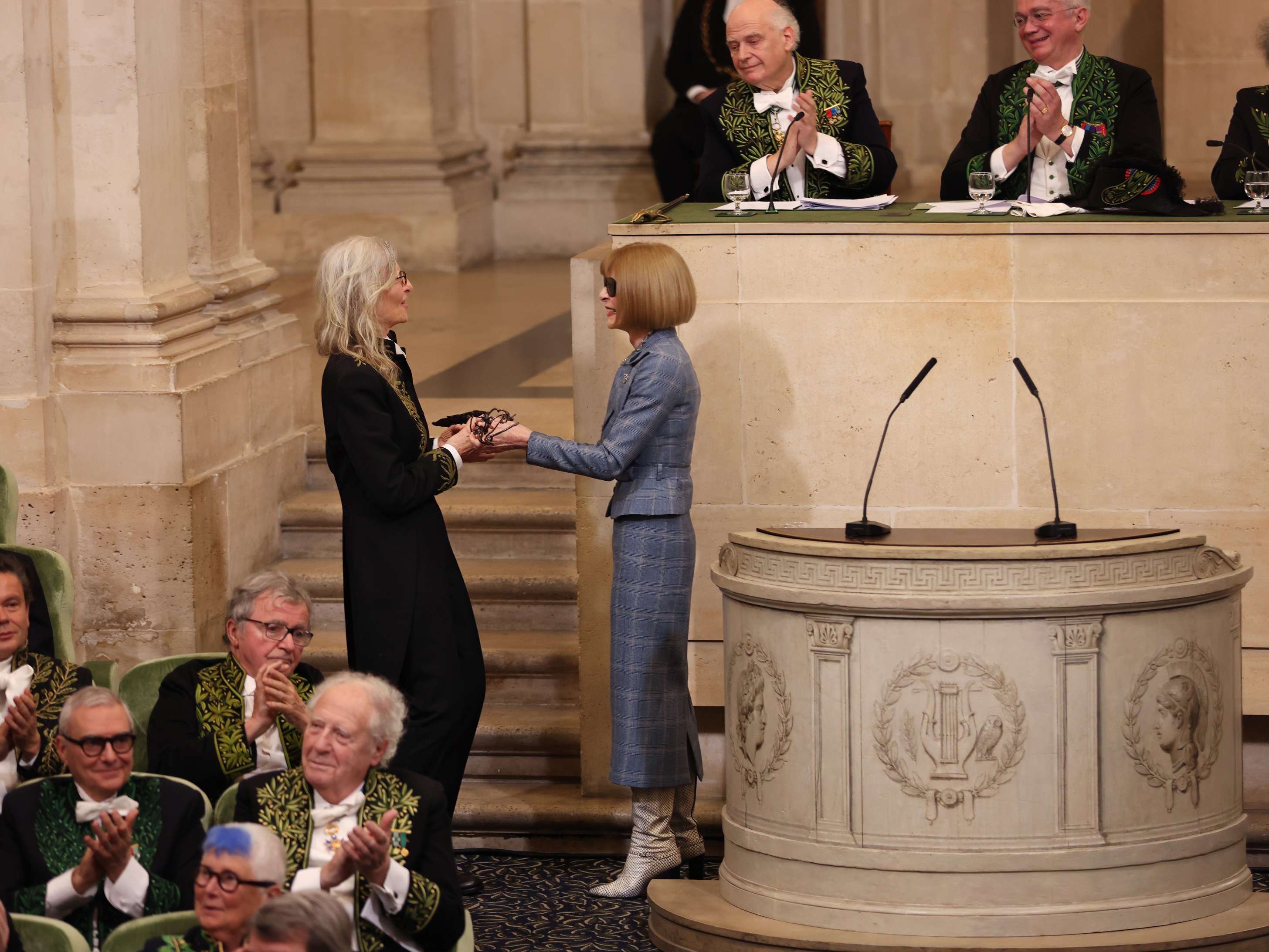 女摄影师Annie Leibovitz（左）于法兰西艺术院外国院士任命典礼中，自Anna Wintour（右）手中接下院士之剑。图／Louis Vuitton提供