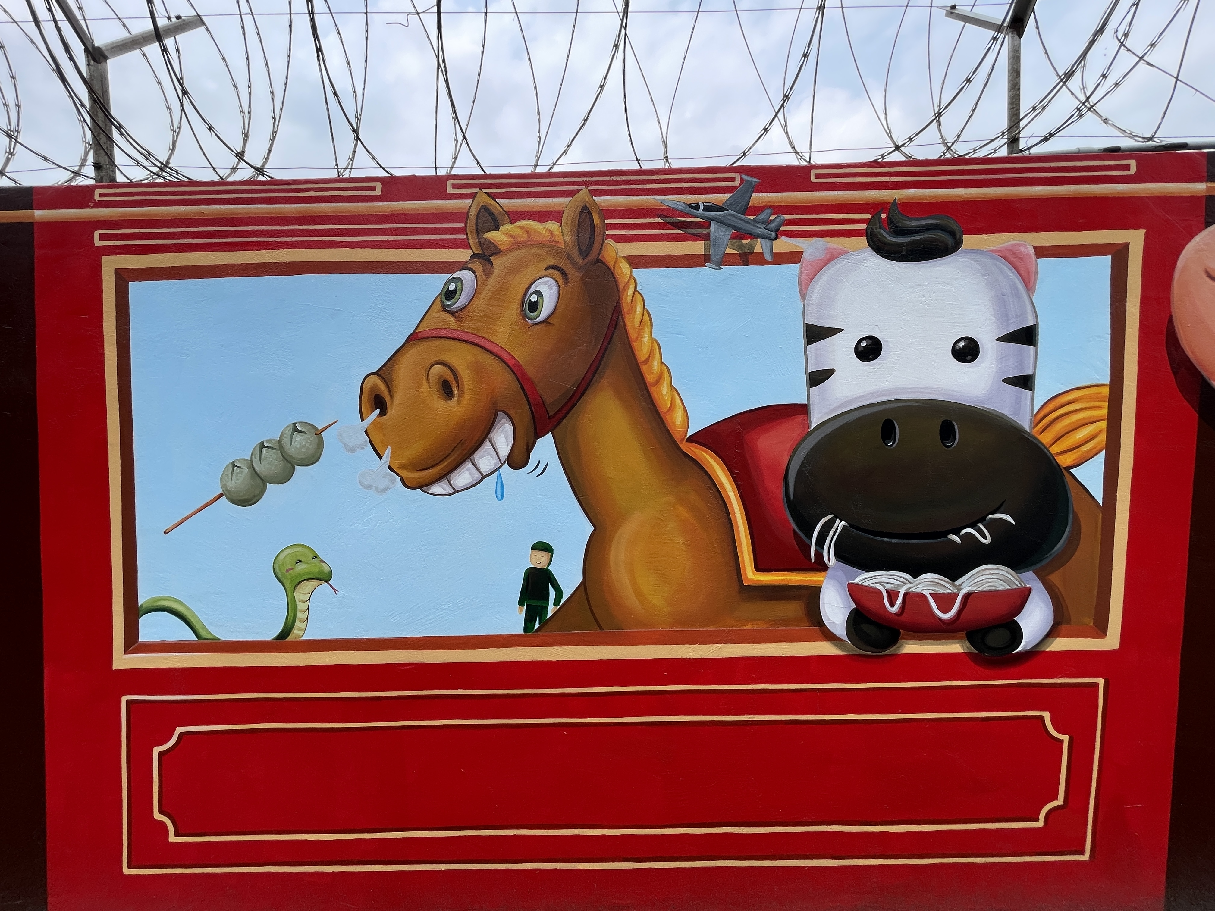 新竹市空军基地旁靠成功路围墙最近完成一大片彩绘，画上以12生肖动物搭铁路小火车的童趣模样、还有米粉跟贡丸。记者张裕珍／摄影