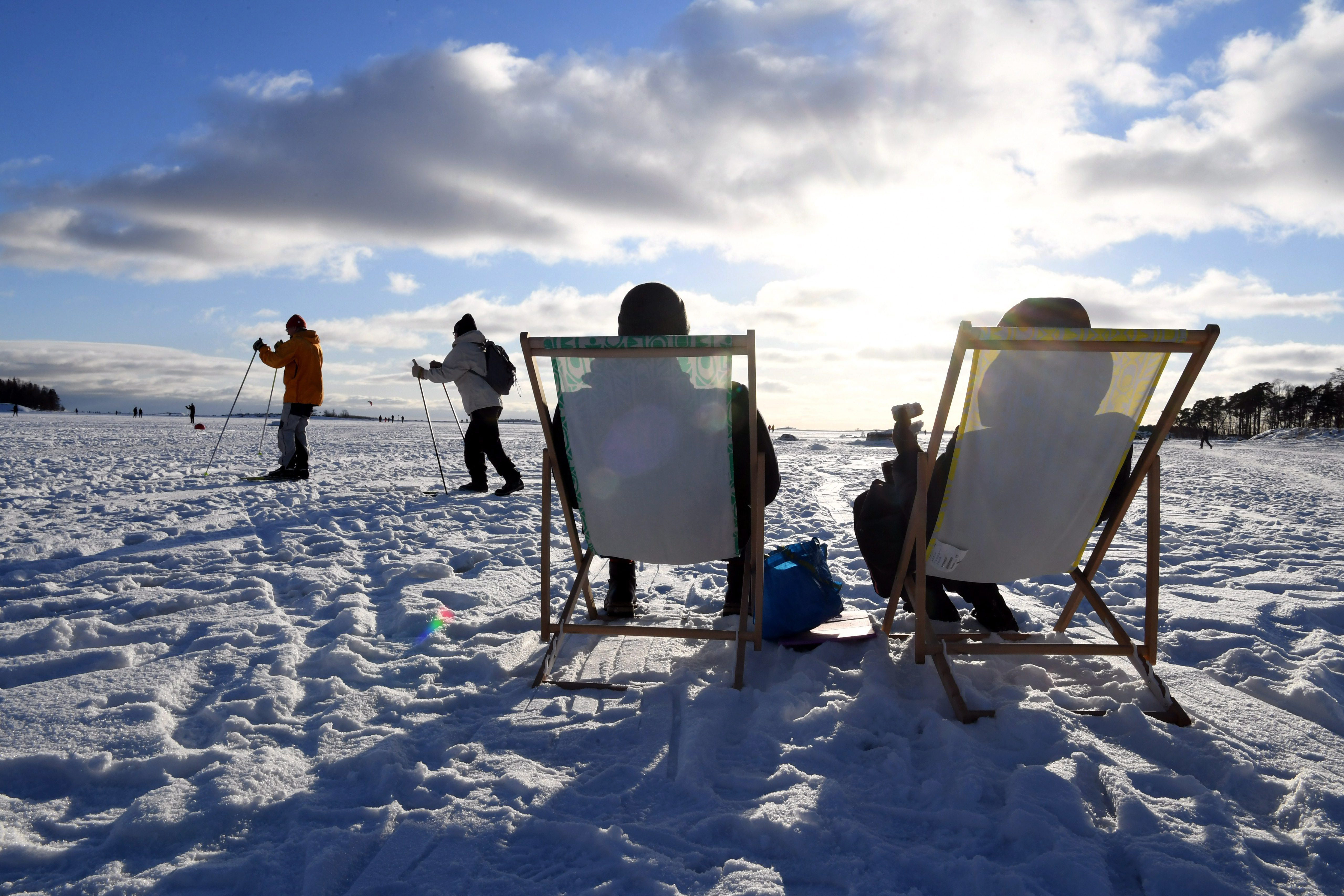 芬兰名列全球最幸福国家第一，图为人们坐在赫尔辛基海滨冰上，其他人滑雪经过。(美联社)