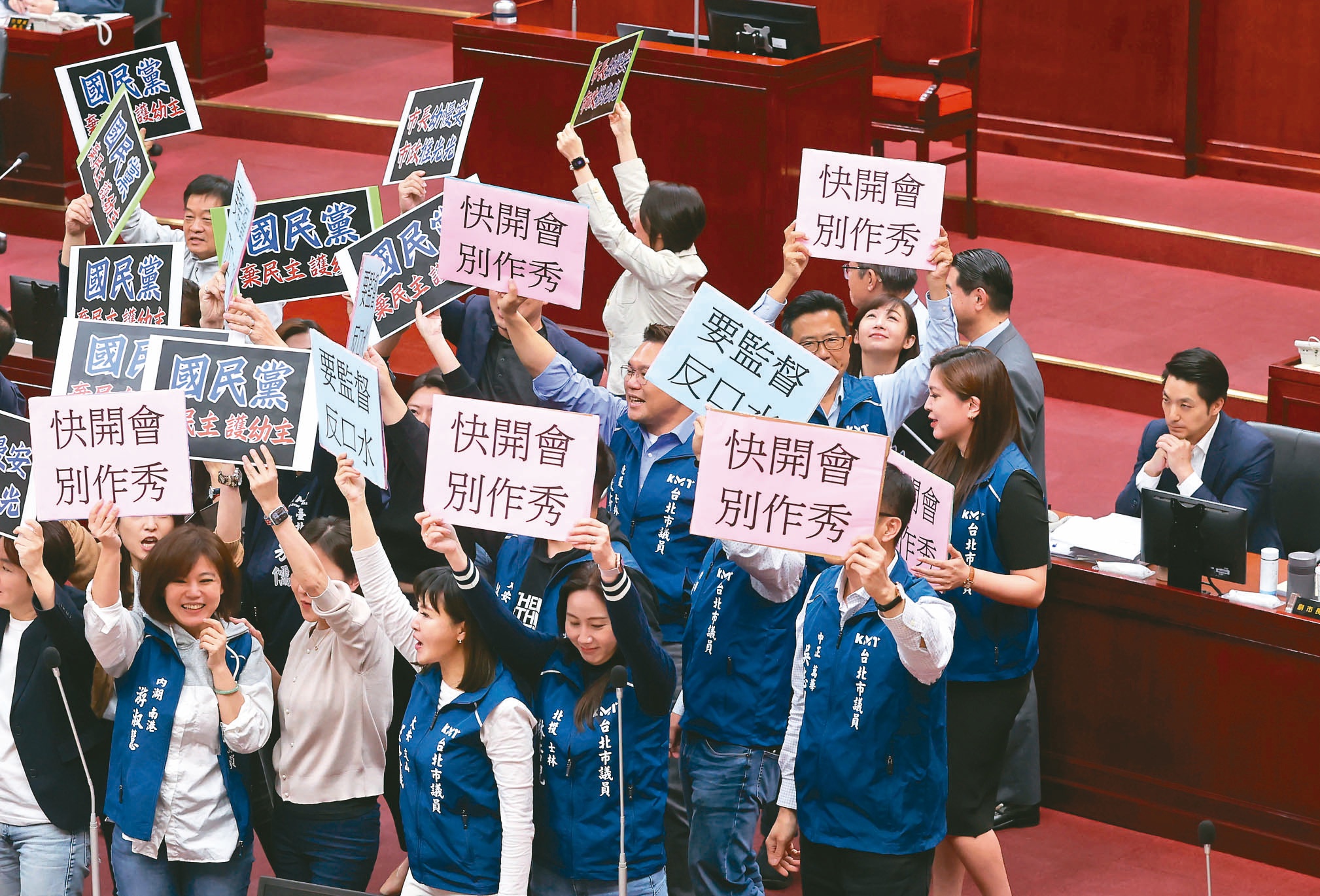 台北市长蒋万安（右）昨赴议会施政报告，民进党议员拿出字牌高喊「国民党弃民主、顾幼主」；国民党议员反击举「快开会、别作秀」，双方吵成一团，坐在备询席的蒋万安面无表情。记者胡经周／摄影