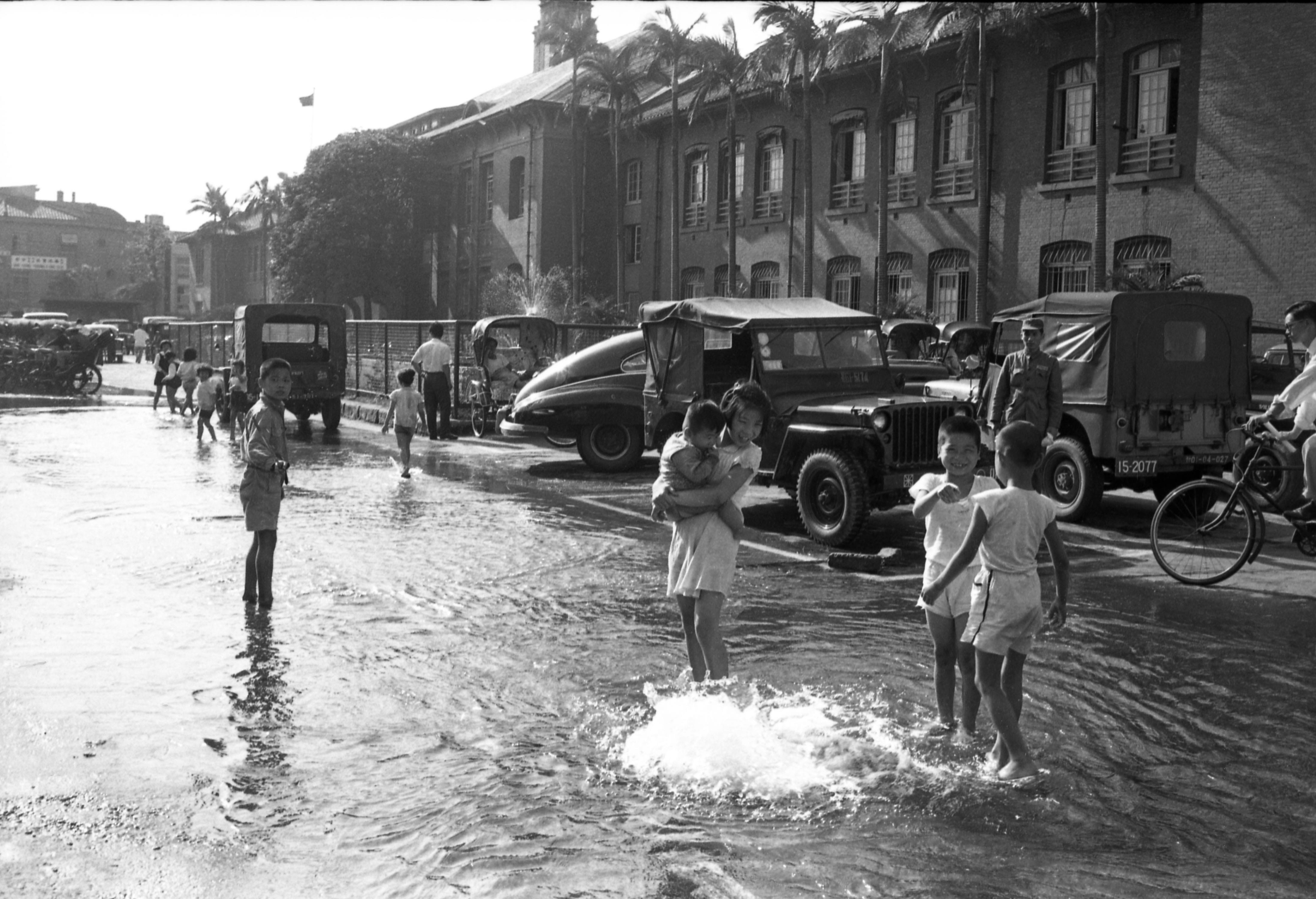 1959年5月8日，台北市长安西路市府大厦门口的自来水管破裂，导致街道积水，附近孩童利用这个机会嬉水避暑。图／联合报系资料照片