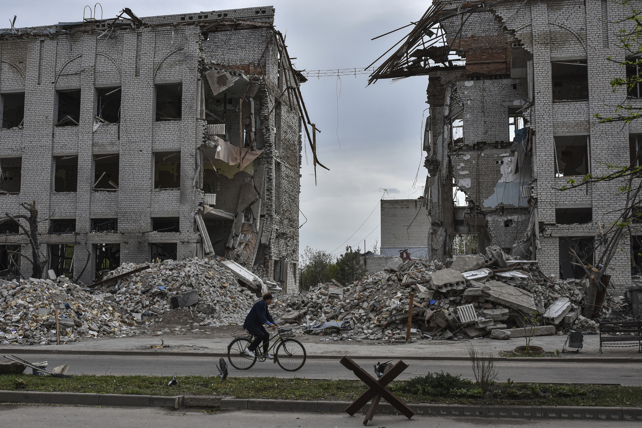 一名妇女18日在乌克兰前线城镇奥里希夫，骑自行车经过一栋被俄罗斯空袭摧毁的建筑物前。(美联社)