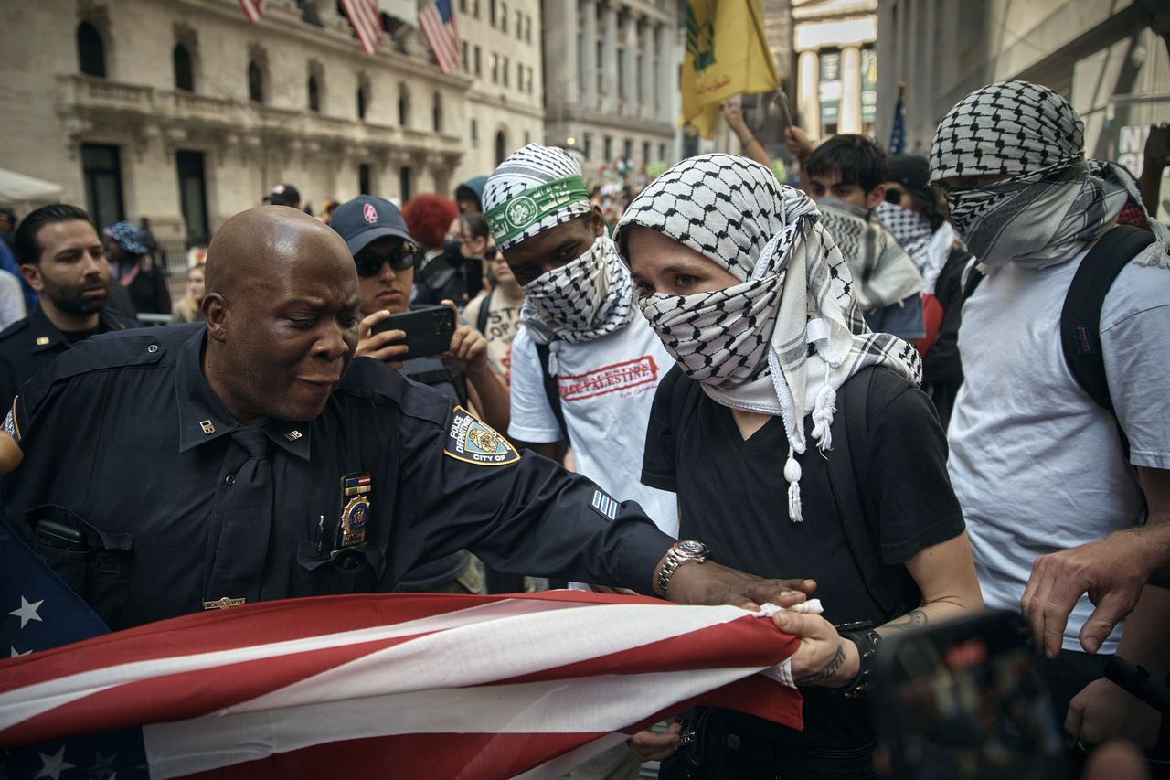 以哈冲突持续不停，拜登府支持以色列政策，引发支持巴勒斯坦的选民不满，全美各地展开示威抗议。图为在支持巴勒斯坦人士本月15日占据纽约市证交所示威时，维安的警员试图制止拉扯美国国旗。美联社