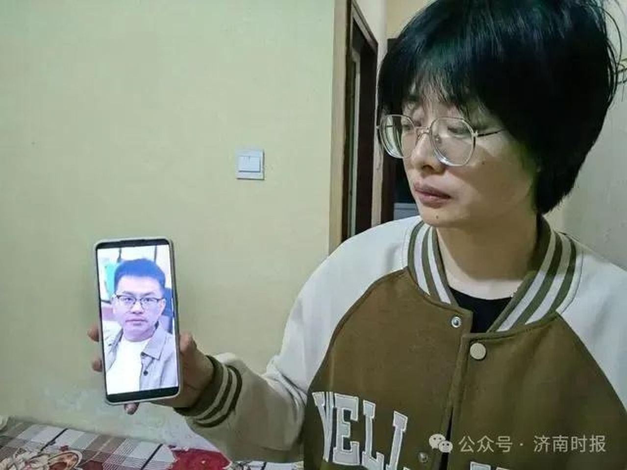 王龙妻子看著手机里的丈夫的照片。(取材自新民周刊)